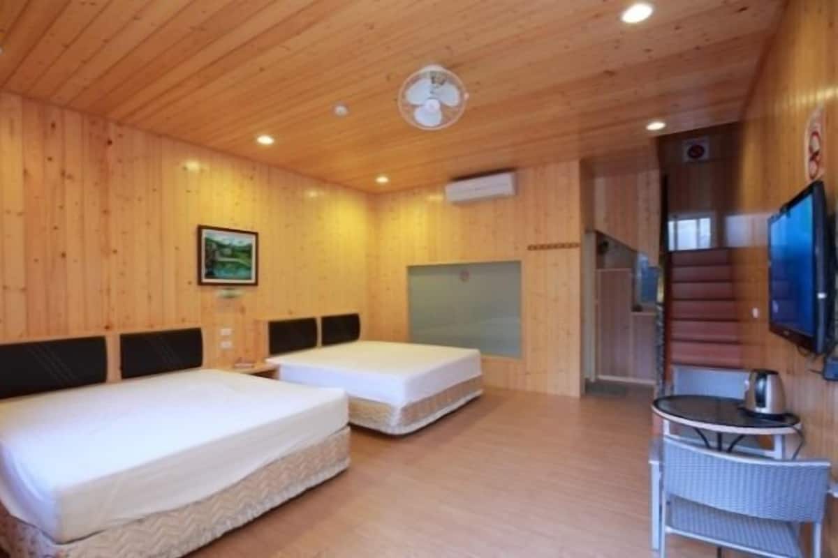 A wooden-paneled room with two beds, a small table, a TV, and a staircase.