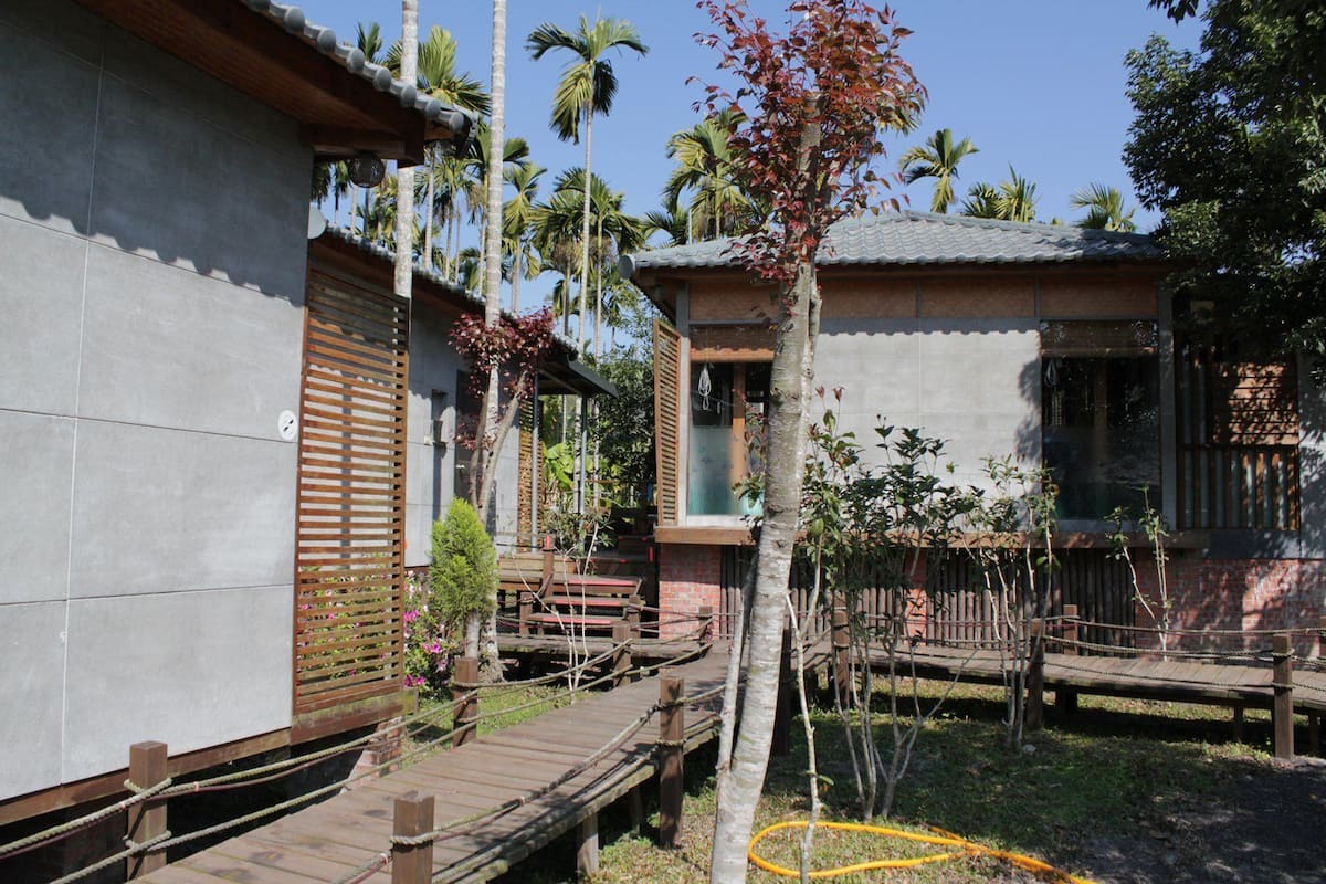 A traditional-style building with a tiled exterior, wooden deck, and a small garden area with benches and a tree.