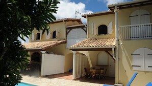 Un edificio de dos pisos con piscina, mobiliario exterior y un patio cubierto.