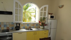 Cocina pequeña con armarios amarillos, una ventana con vistas a palmeras, un microondas y un lavabo.