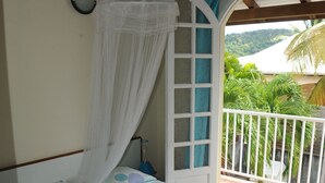 Una cama con dosel, una puerta blanca y vistas a la vegetación exterior.