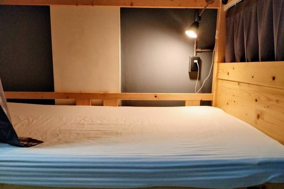 A bunk bed with a wooden headboard, a wall-mounted light, and a power outlet.
