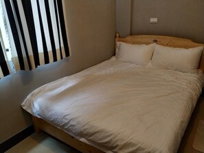 A single bed with a wooden headboard and white bedding in a room with plain walls and a window with vertical blinds. - Backpack Home 497 No.2 (Jincheng)