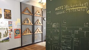 Una habitación con piso de madera, una pizarra con información sobre WiFi y contraseña, y varios carteles en la pared.