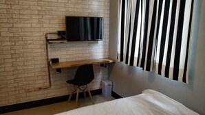 Una habitación con pared de ladrillo, televisor montado, escritorio con silla y cama.