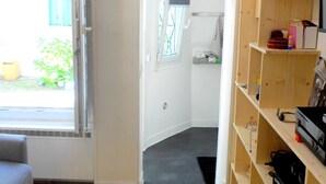 Una habitación con piso de madera, una puerta blanca que da a un baño y una ventana con vistas a la vegetación.