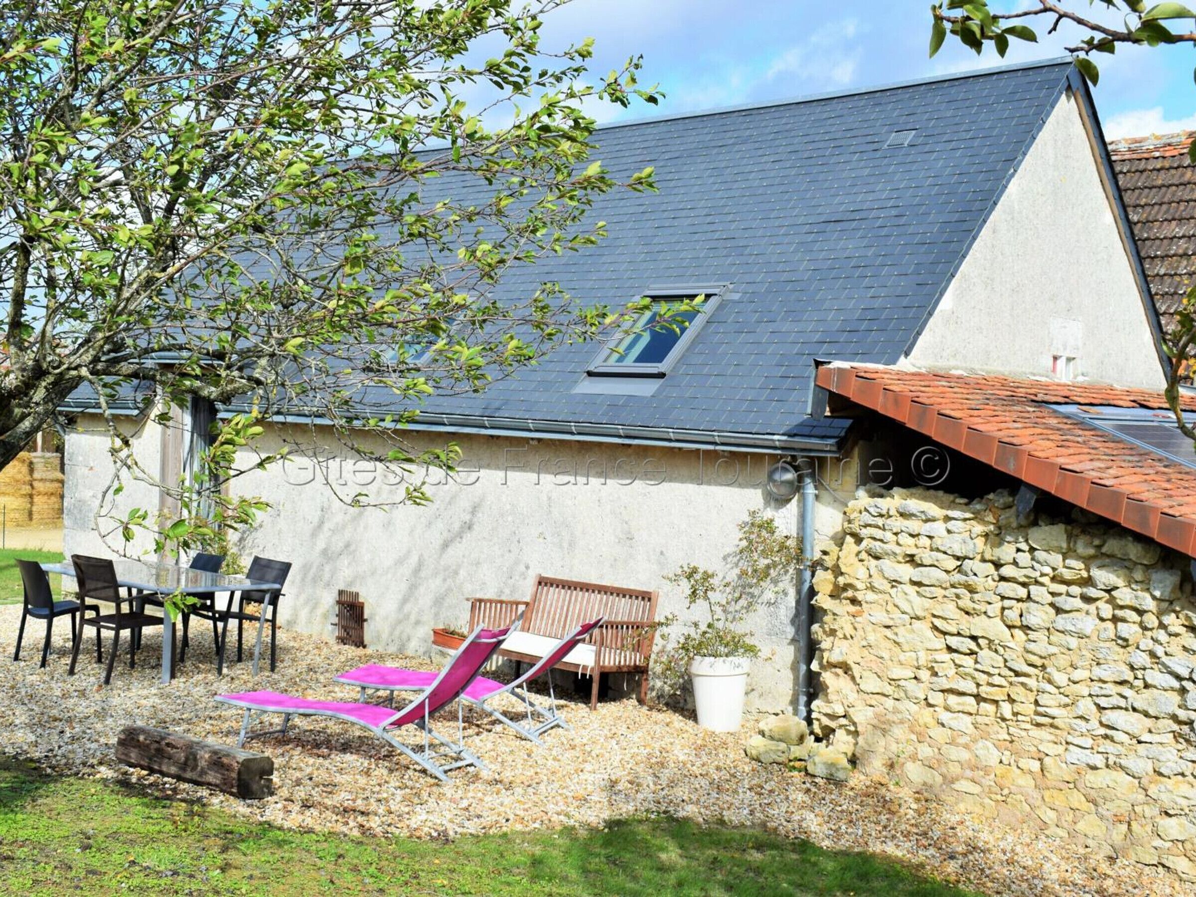 Ein Haus mit geneigtem Dach, einer Steinwand und einer Terrasse mit Gartenmöbeln.