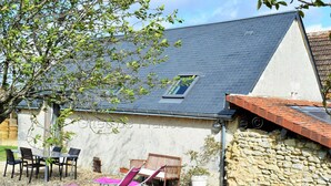 Une maison avec un toit en pente, un mur en pierre et un patio aménagé avec du mobilier d’extérieur.