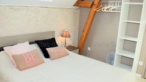Une chambre avec un plafond en pente, un lit avec une literie à motifs, une lampe de chevet et une armoire blanche.