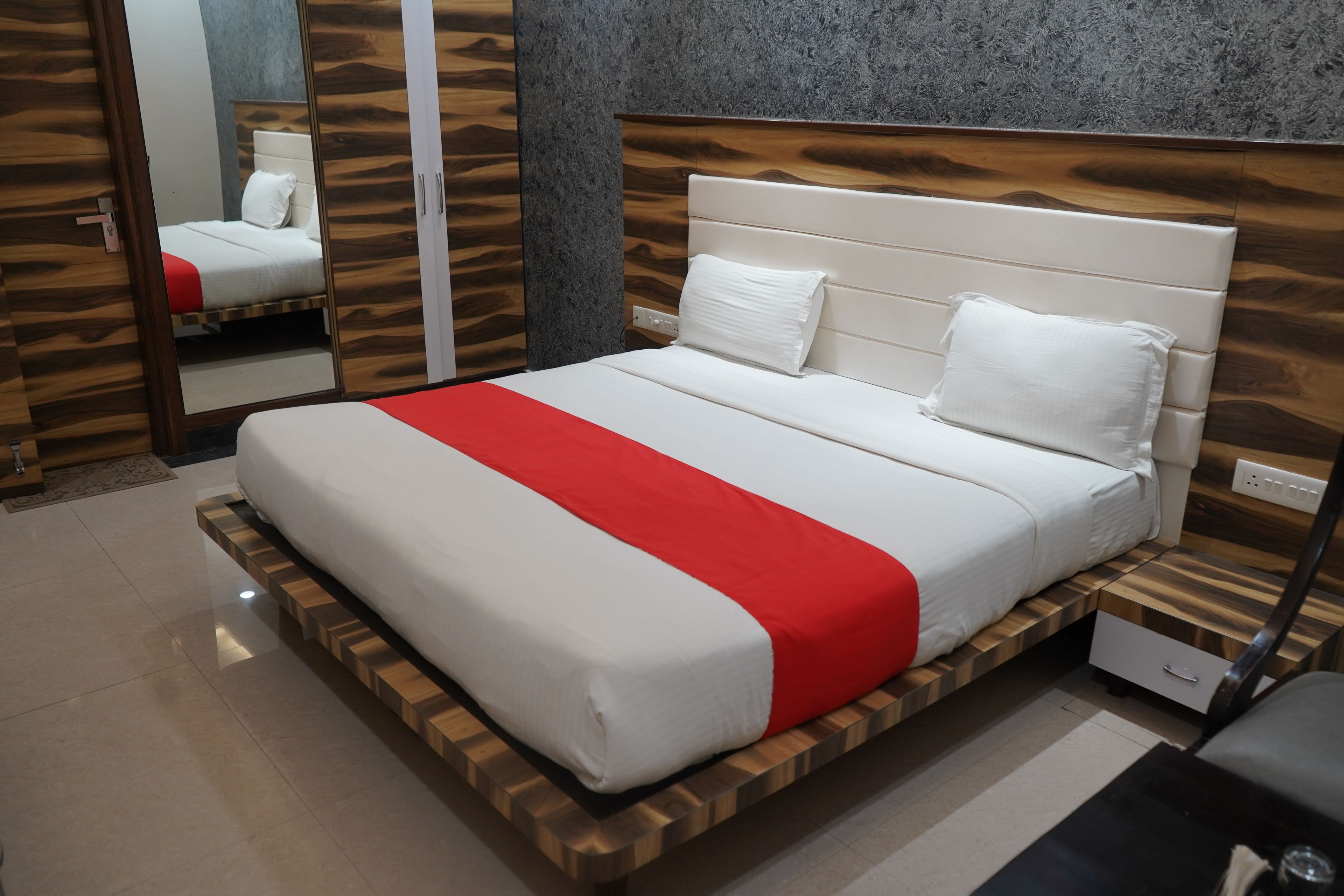 Ein modernes Hotelzimmer mit einem Bettgestell aus Holz, einer roten und weißen Bettdecke und einem Nachttisch mit einer Schublade.