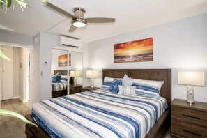 Ein Schlafzimmer mit Bett, Nachttischen, Deckenventilator, einem Gemälde und einer Klimaanlage.