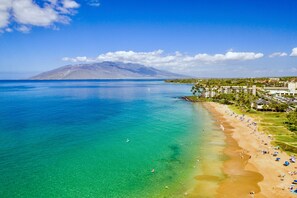 Ein Küstenstrand mit klarem türkisblauem Wasser, einem sandigen Ufer und einem Berg im Hintergrund.