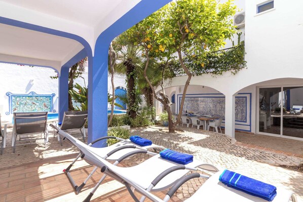 A sunlit outdoor lounge area with lounge chairs and a tree. - Villa Oasis, Hidden Gem, Heart of Village, Pool & Courtyard (carvoeiro)