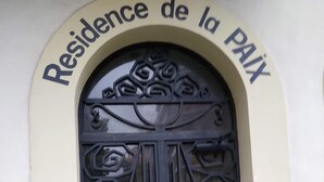 Una reja de hierro forjado negra con diseños intrincados, ubicada en una entrada en arco con la inscripción 'Residence de la Paix'.