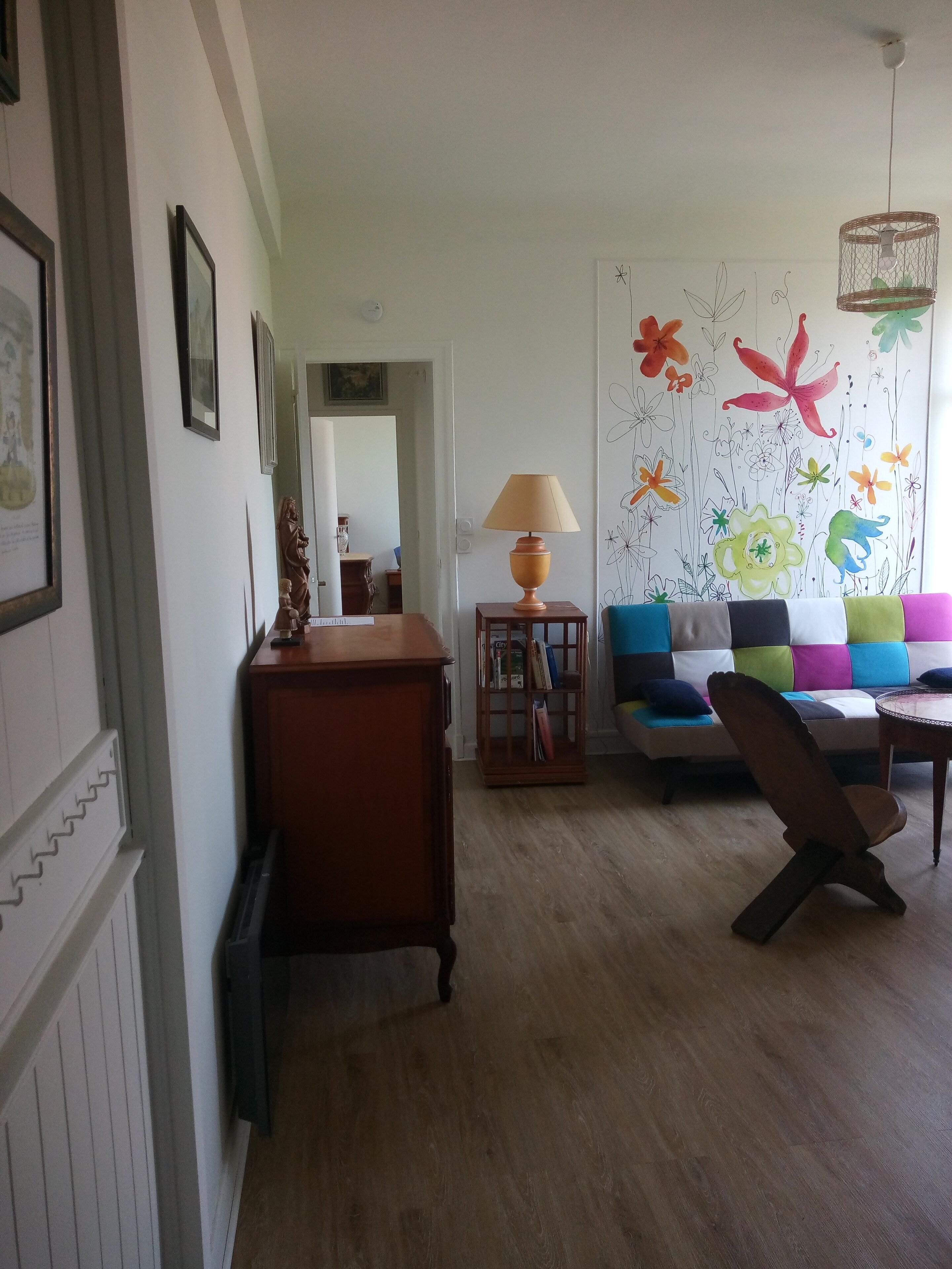 Una sala de estar con un aparador de madera, una lámpara, un sofá colorido y una pared con diseños florales.