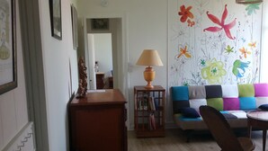 Una sala de estar con un aparador de madera, una lámpara, un sofá colorido y una pared con diseños florales.