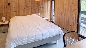 A modern bedroom with a large bed, wooden panel walls, a wooden table, and a window with a view. - 1 RR6171 - (Megève)