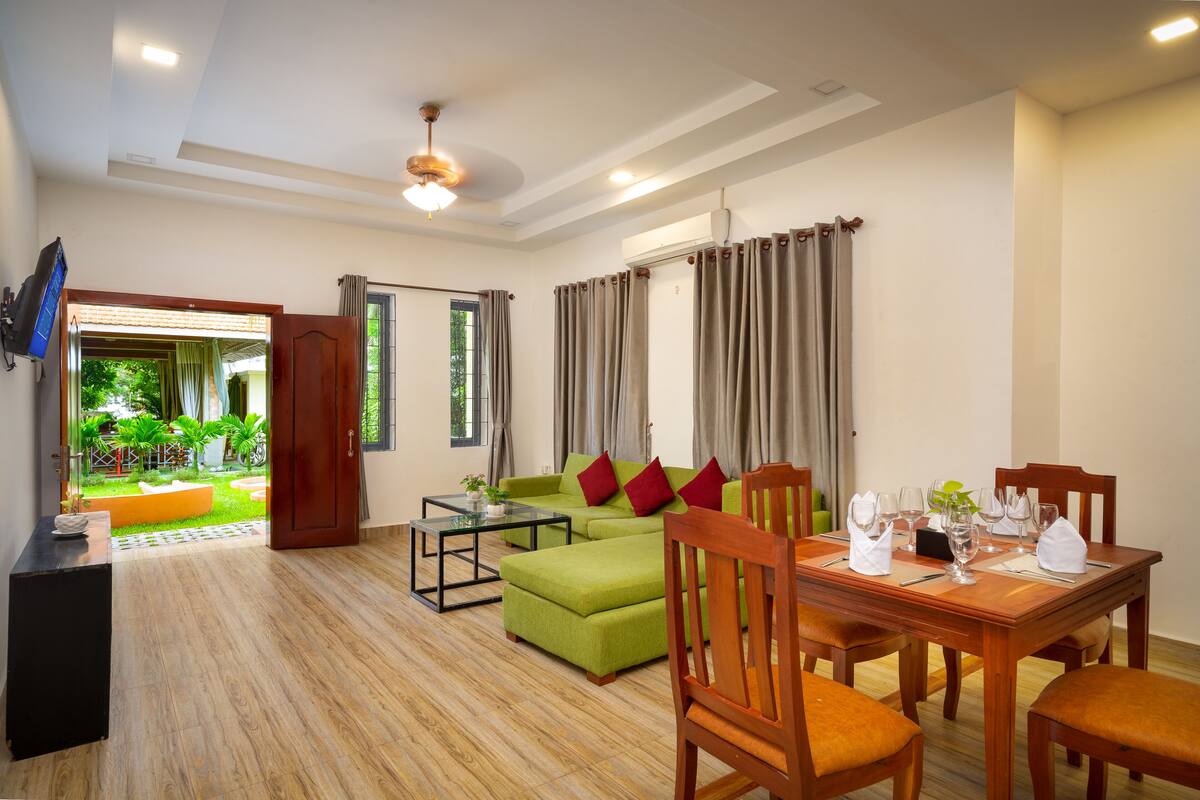 Un salón moderno con un sofá verde, una mesa de comedor de madera y un televisor montado en la pared.