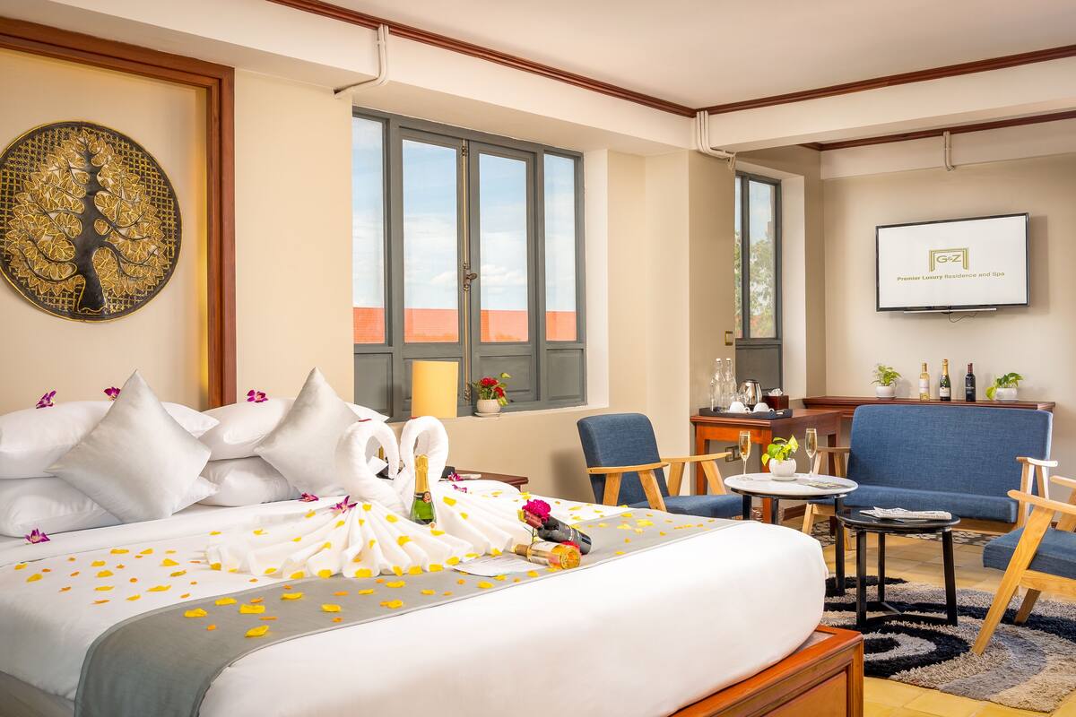 Habitación de hotel con cama, dos sillas, una mesita, televisión y balcón con vistas.