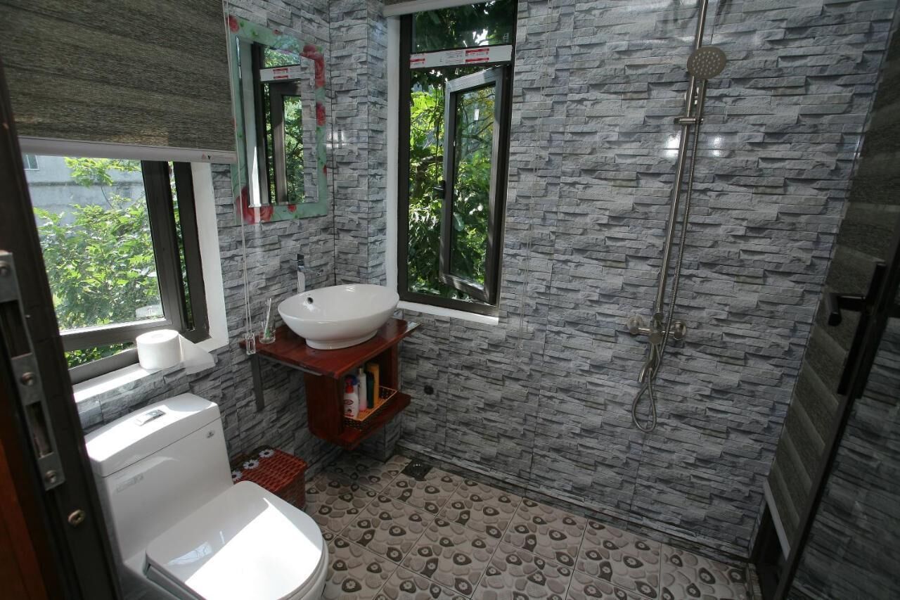 A bathroom with a white sink, a toilet, a shower, and a window with a view of greenery.
