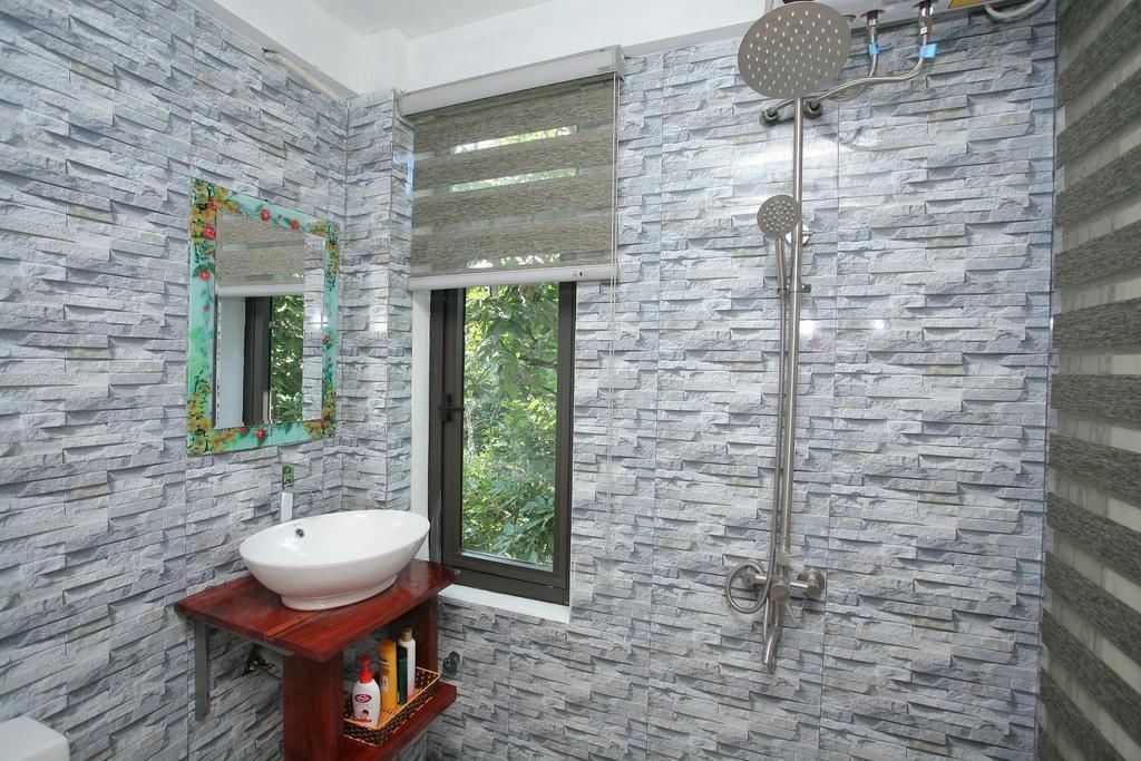 A bathroom with a stone-textured wall, a white sink, a mirror with a floral frame, and a shower with a rain showerhead.