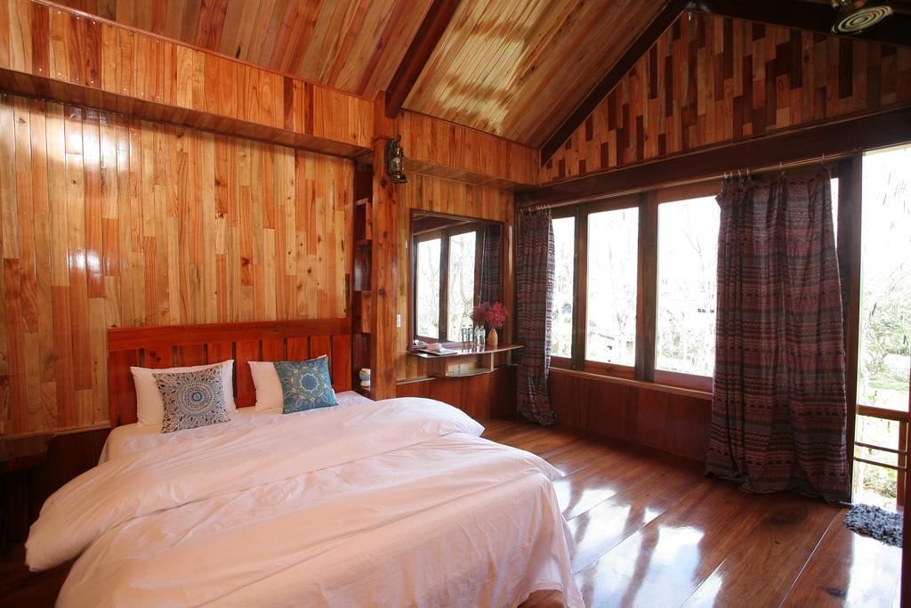Un dormitorio de cabaña de madera con una cama grande, paredes de madera y ventanas amplias.