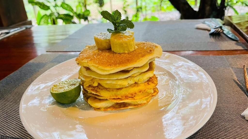 A stack of pancakes on a plate with a lime wedge and a mint leaf on top.