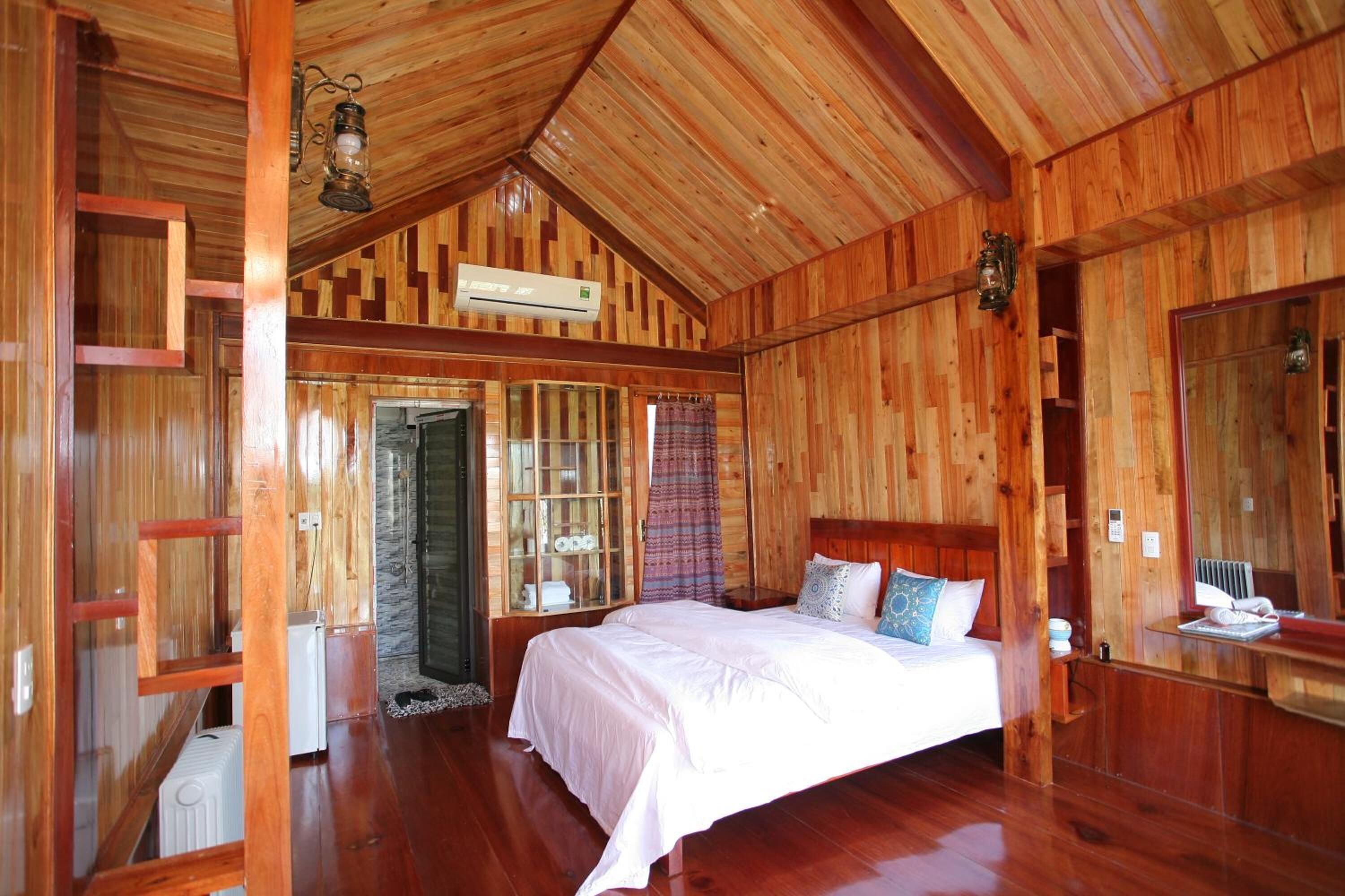 A wooden cabin bedroom with a bed, a mirror, and a window.