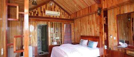 A wooden cabin bedroom with a bed, a mirror, and a window.
