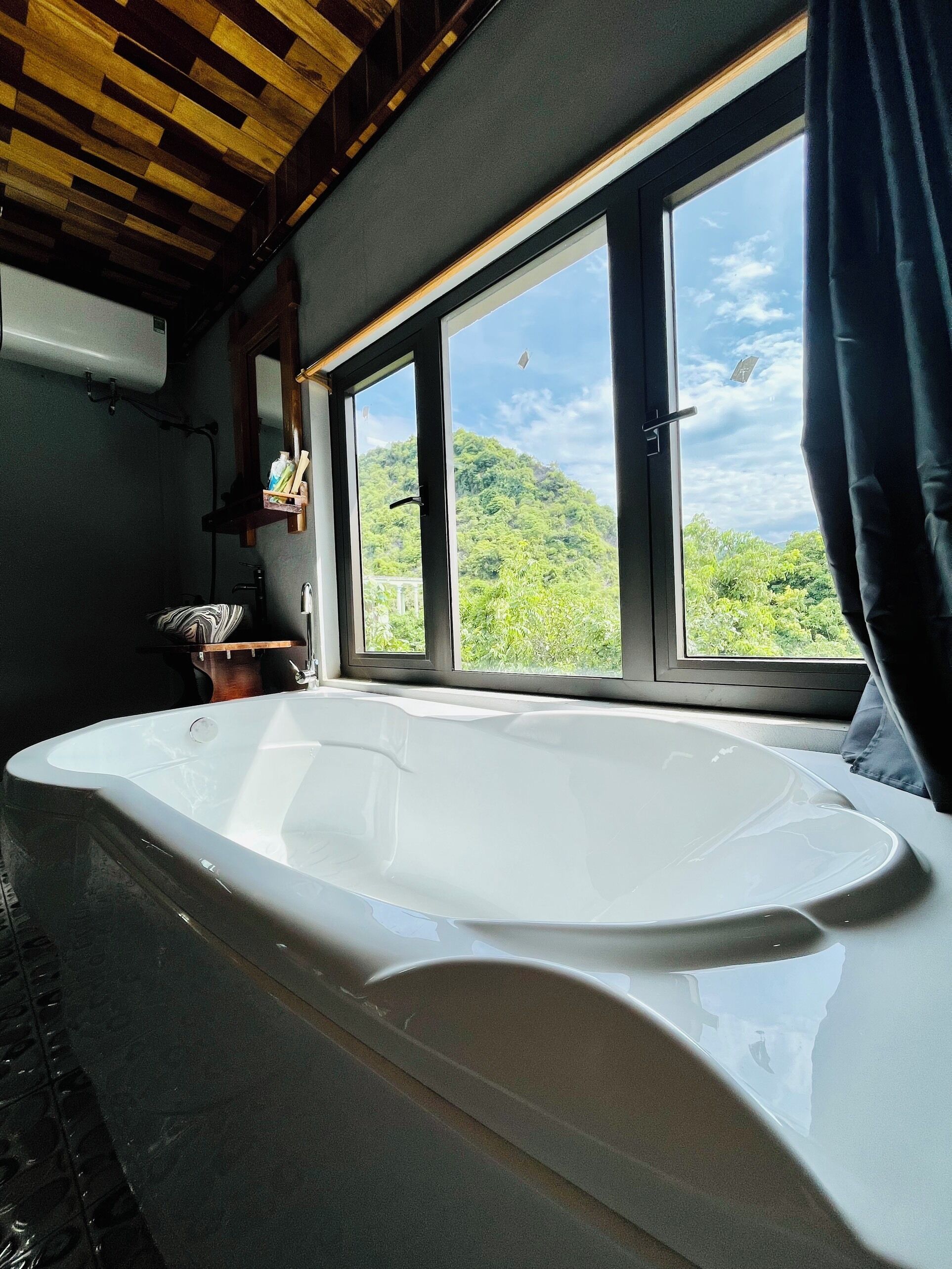 Un baño con una bañera grande, una ventana que da a vistas de follaje y un techo de madera.