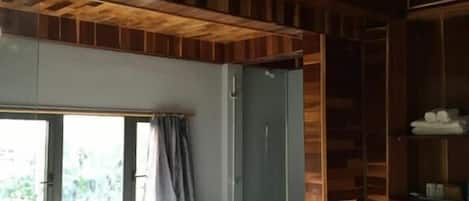 A room with a bathtub, a window, a shower, and a bedside table with a lamp.