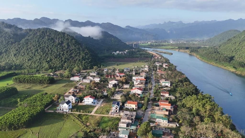 A river running alongside a small village with houses and greenery.