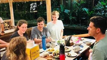 A group of people dining at a wooden table with a thatched roof, surrounded by lush greenery.