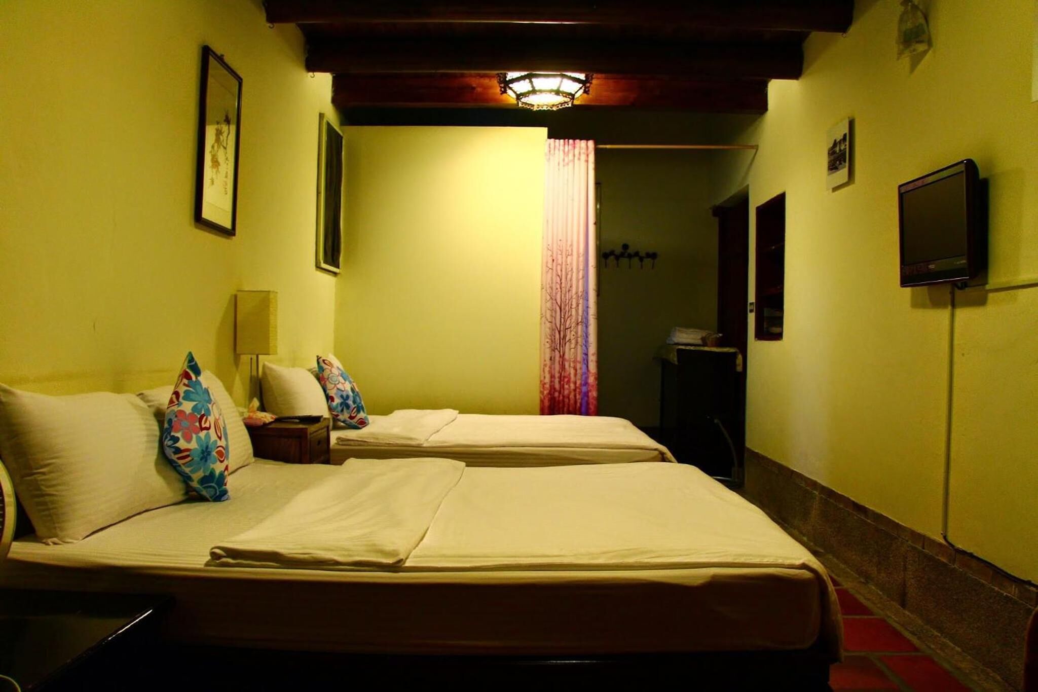 A hotel room with two beds, a TV, and a lamp.