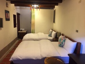 Une chambre d’hôtel avec deux lits, une tête de lit en bois, une petite table et une chaise en osier.