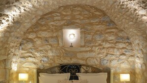 A bedroom with a stone arch ceiling, a large bed with multiple pillows, bedside lamps, and a wooden bench. - Olea (East Mani)