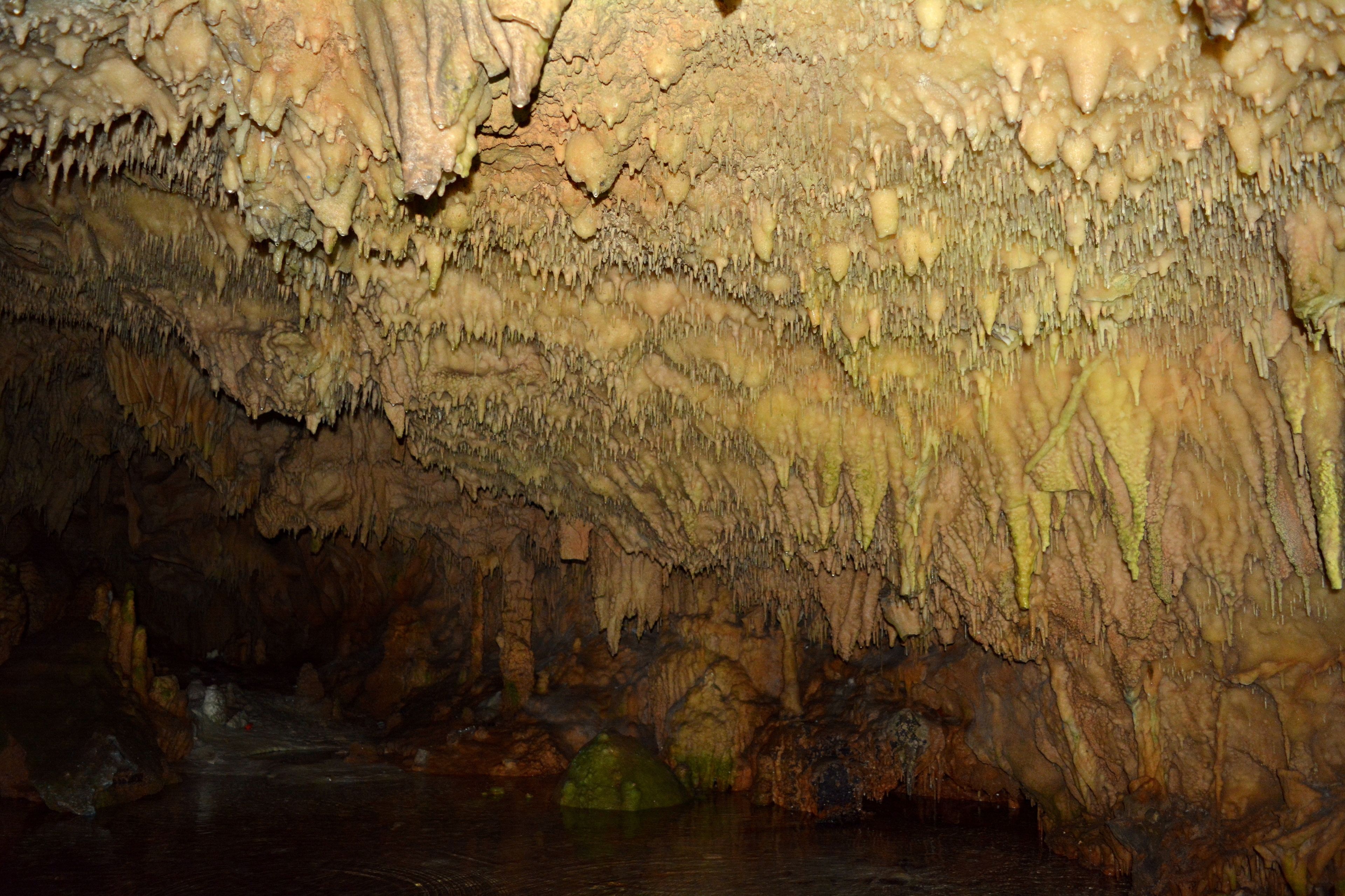 A cave with stalactites and stalagmites, water flow, and a greenish mineral deposit.