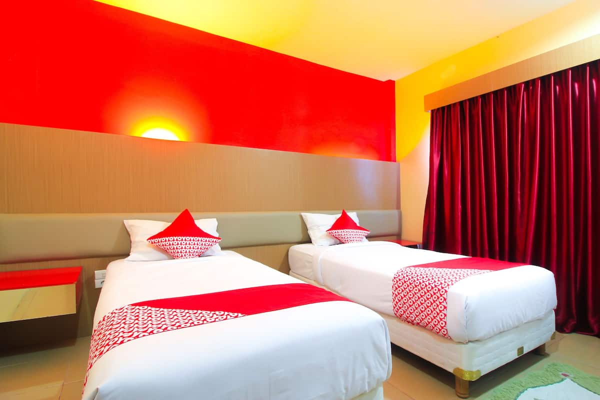 Ein Hotelzimmer mit zwei Betten, roter und weißer Bettwäsche, einem roten Vorhang und einer Wandleuchte.