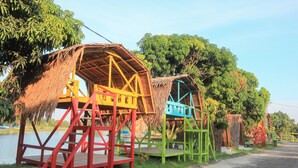 A series of colorful wooden structures with thatched roofs by a body of water. - OYO 1153 Tiga Dara Hotel & Resort Syariah (Pekanbaru)