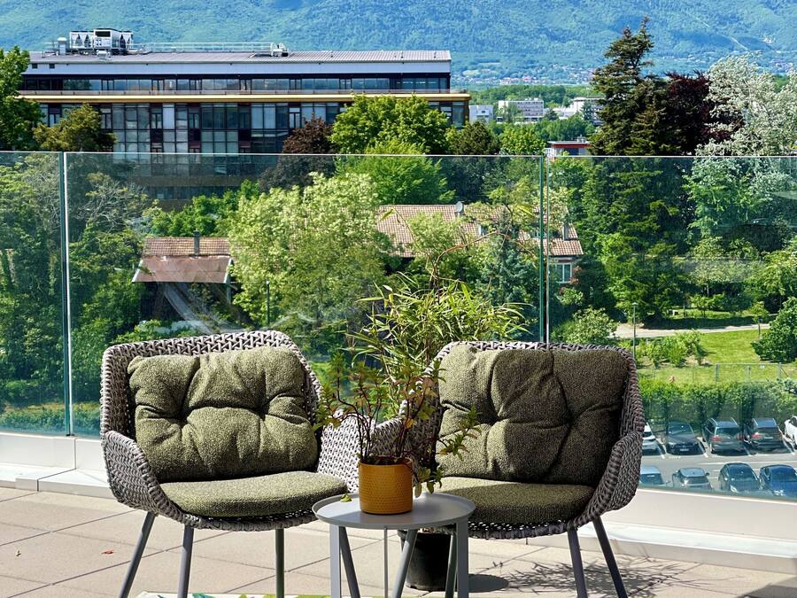 Un balcon avec deux fauteuils rembourrés, une petite table et une plante en pot.