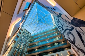 A modern building with a glass atrium and a large mural. - Mercure Geneva Airport  (Meyrin)