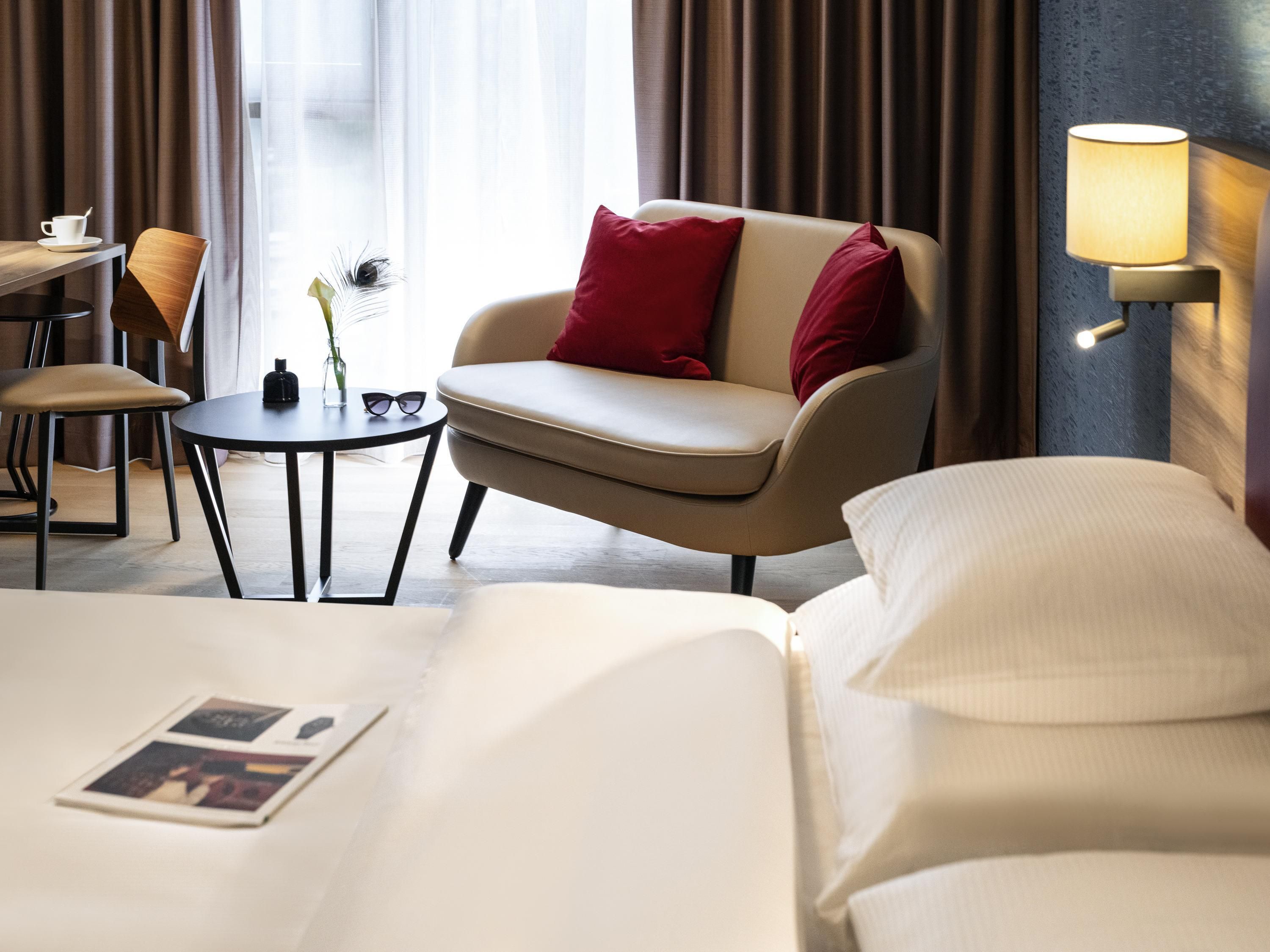 Una habitación de hotel con cama, sofá, mesita y lámpara.