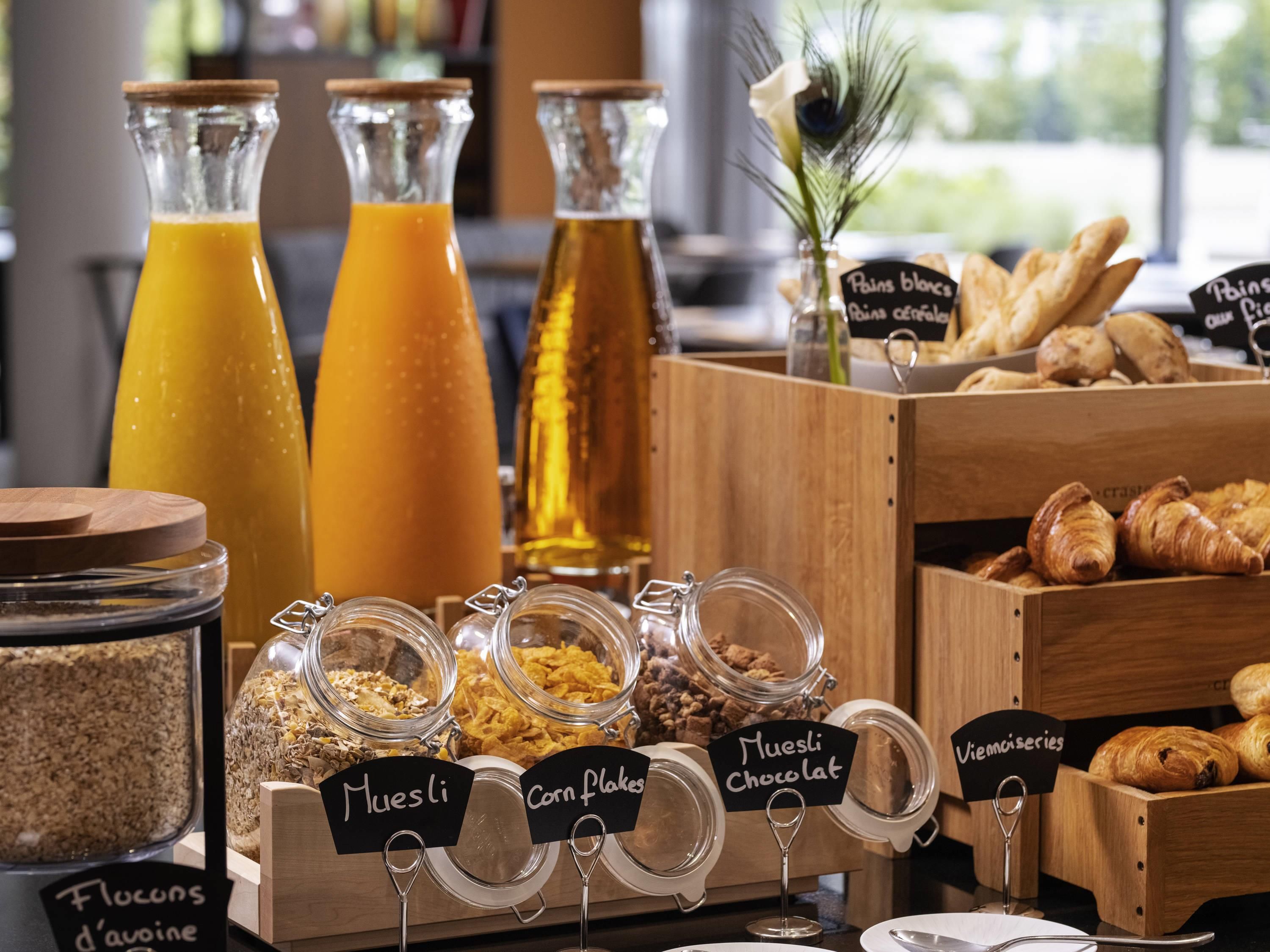 Un bufé de desayuno con alimentos identificados, incluyendo muesli, copos de maíz y chocolate.