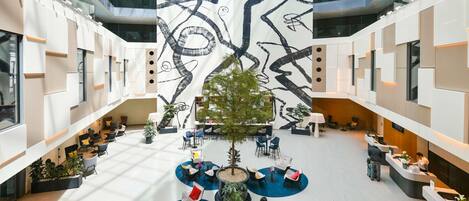 A modern atrium with a central seating area, multiple levels, and a large abstract mural.