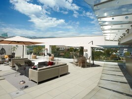 Una terraza en la azotea con mobiliario exterior, sombrillas y vistas del paisaje circundante.