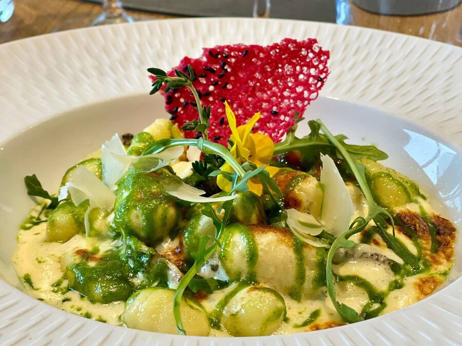 Ein weißer Teller mit einer Speise, garniert mit Grünzeug, Blumen und einer roten Frucht.