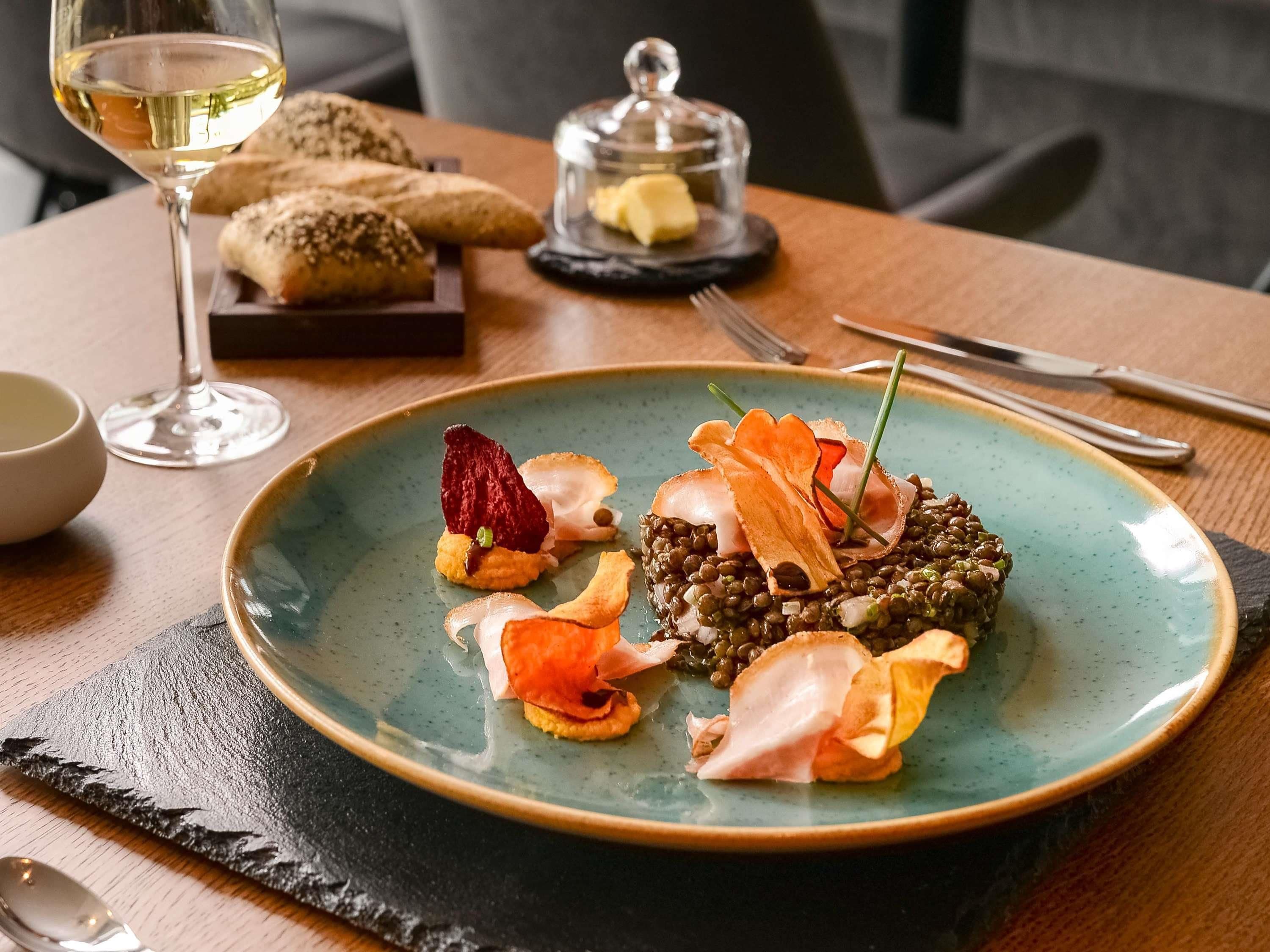 Ein Teller Essen mit einem Glas Weißwein, Brot und einer Butterdelle auf einem Tisch.