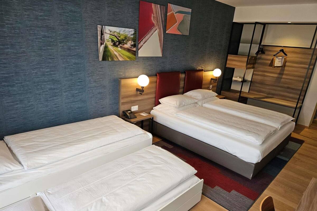 A hotel room with two beds, a nightstand with a lamp, a phone, and artwork on the wall.