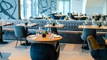 A modern restaurant with round tables, grey upholstered seating, and a minimalist decor.