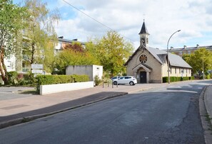 A church with a steeple and a clock, a white car parked in front, and a residential building in the background. - Apartment in Nevers for 6 to 8 people (Nevers)